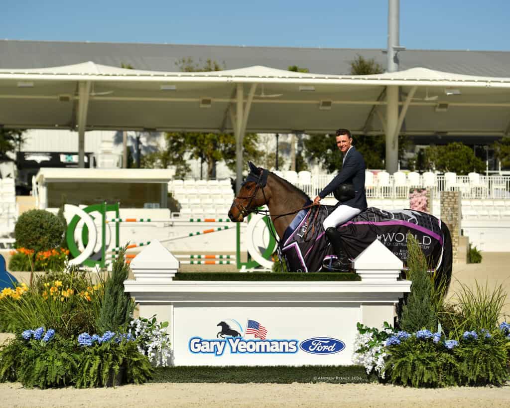 A rider in formal attire sits on a horse draped in a branded sheet, positioned behind a sign reading "Gary Yeomans Ford" at an outdoor equestrian event.