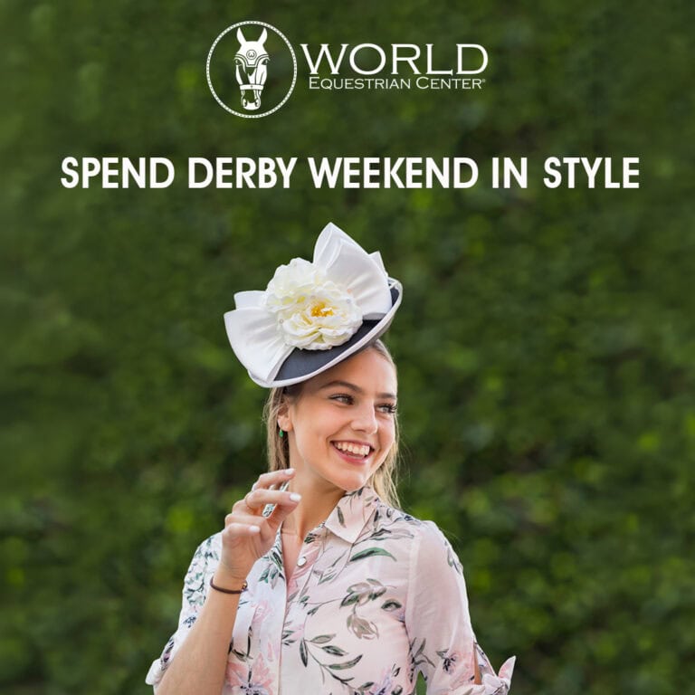 A woman in a floral shirt and decorative hat smiles outdoors under a sign that reads 