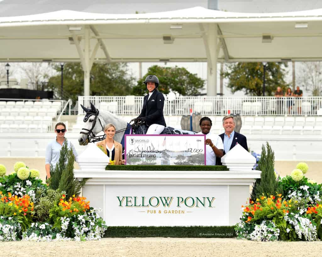 A rider on a horse holds a large check while posing with four people at a podium labeled "Yellow Pony Pub & Garden" in an outdoor arena.