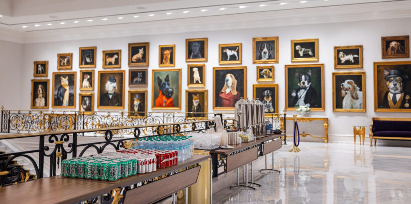 A gallery wall displays framed dog portraits in a bright, elegant room with a refreshment table set up in the foreground.