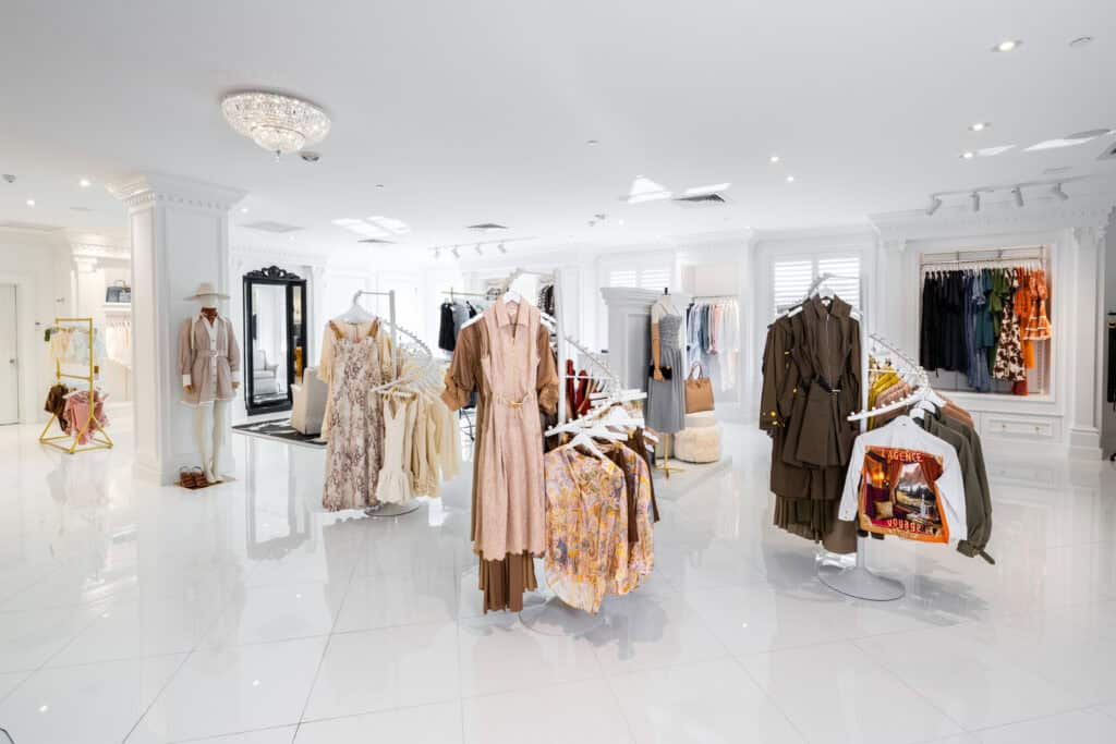 Bright, modern clothing boutique with white tile floors, racks of dresses and outfits, mirrors, and organized displays of women's apparel.