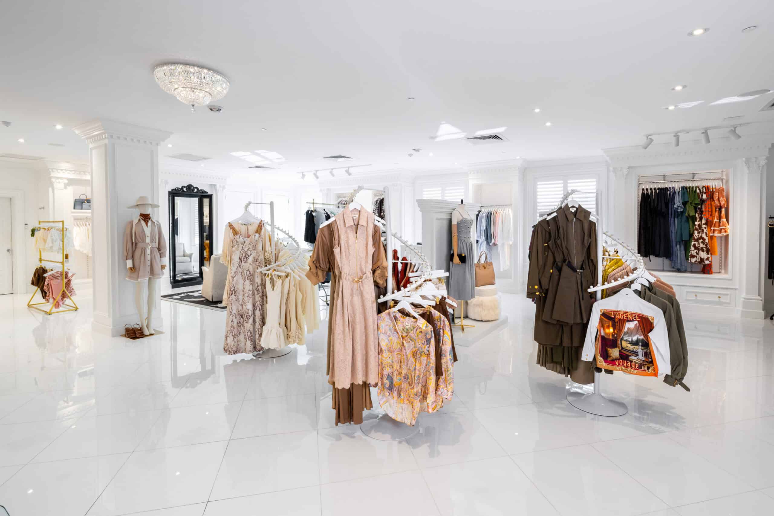Bright, modern clothing boutique with white tile floors, racks of dresses and outfits, mirrors, and organized displays of women's apparel.