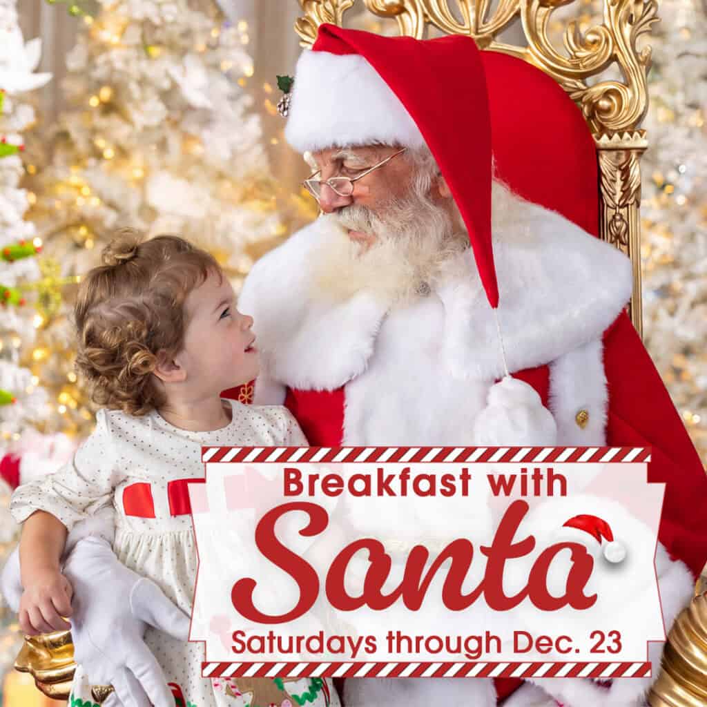A child sits on Santa’s lap, both smiling, surrounded by Christmas decorations. A sign reads, “Breakfast with Santa, Saturdays through Dec. 23.”.