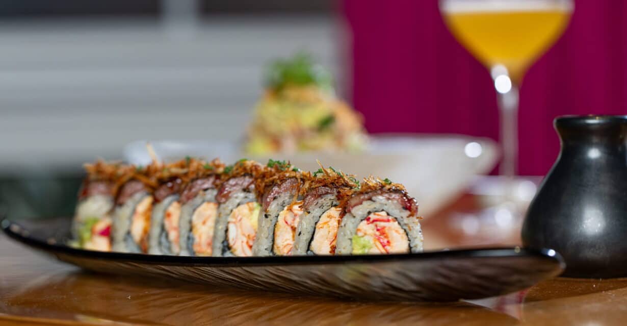 Sushi roll served with a cocktail and salad in the background
