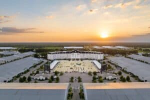 Aerial view of a large white hotel with a courtyard, surrounded by event tents and greenery, at sunset.
