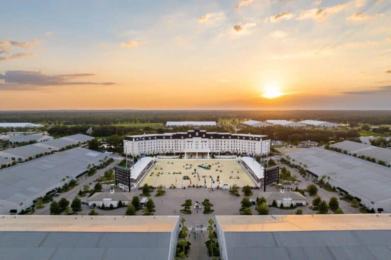 Aerial view of a large white hotel with a courtyard, surrounded by event tents and greenery, at sunset.