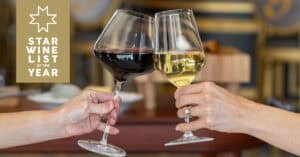 Two hands clink wine glasses, one with red wine and one with white wine; a 