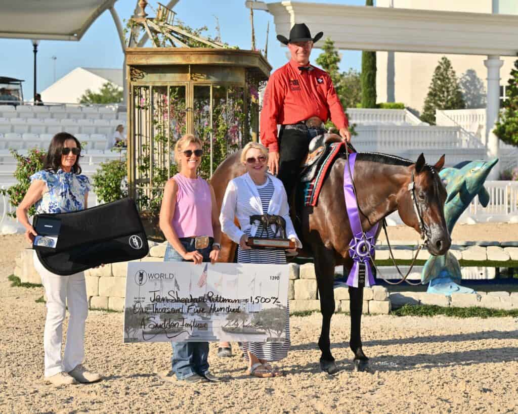 Four people and a horse pose outdoors; one person on horseback holds a ribbon, while others hold a large check, a trophy, and a guitar case.