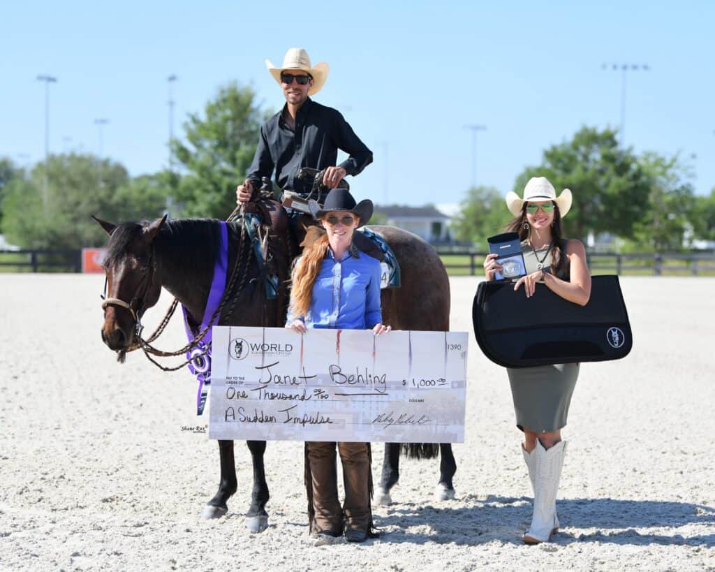 Three people pose outdoors with a horse. One is on horseback, and two stand holding a large check, a plaque, and an award case. All are wearing cowboy hats and formal western attire.