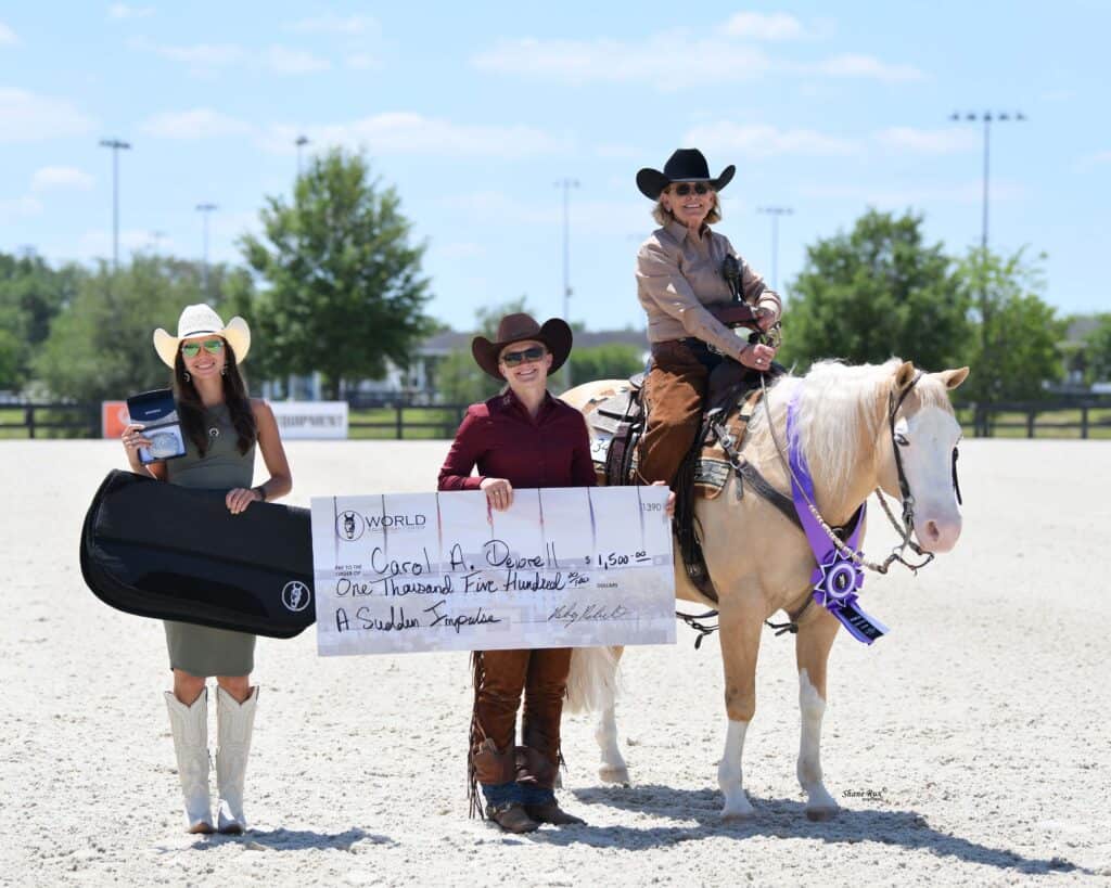 Three people pose outdoors; one on horseback with a purple ribbon, another holding a large check, and the third holding a prize case. The scene is at a horse event.