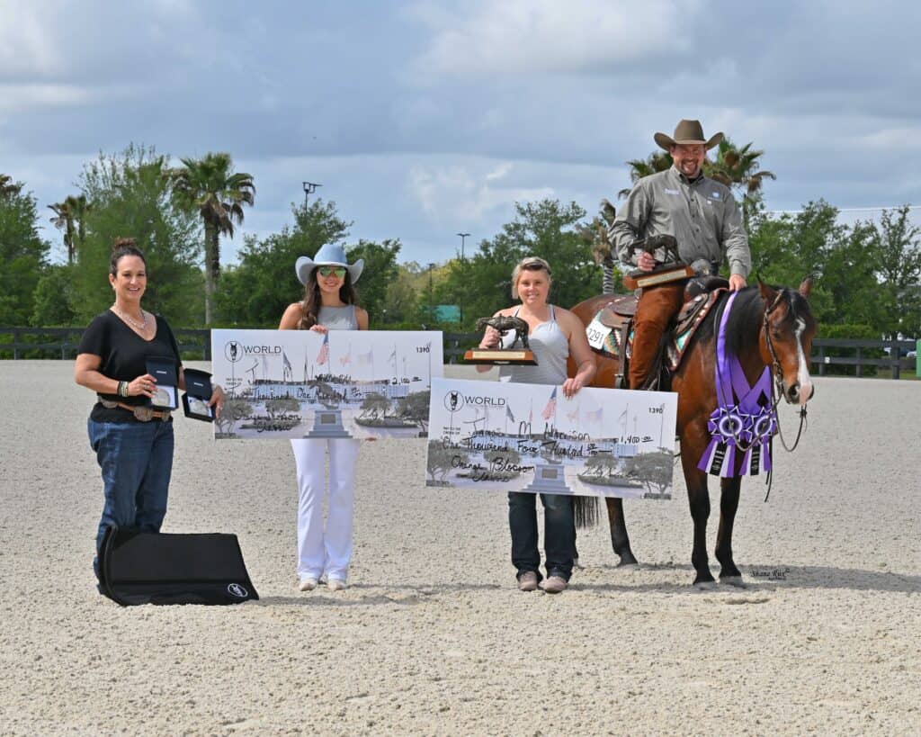 Four people pose outdoors with awards; two hold large checks, one stands with a trophy, and one sits on a horse adorned with ribbons. Trees and clouds are visible in the background.