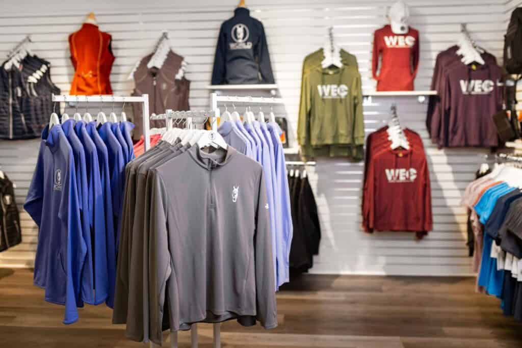 Clothing store display with jackets, sweatshirts, and shirts in various colors hanging on racks and wall hooks.