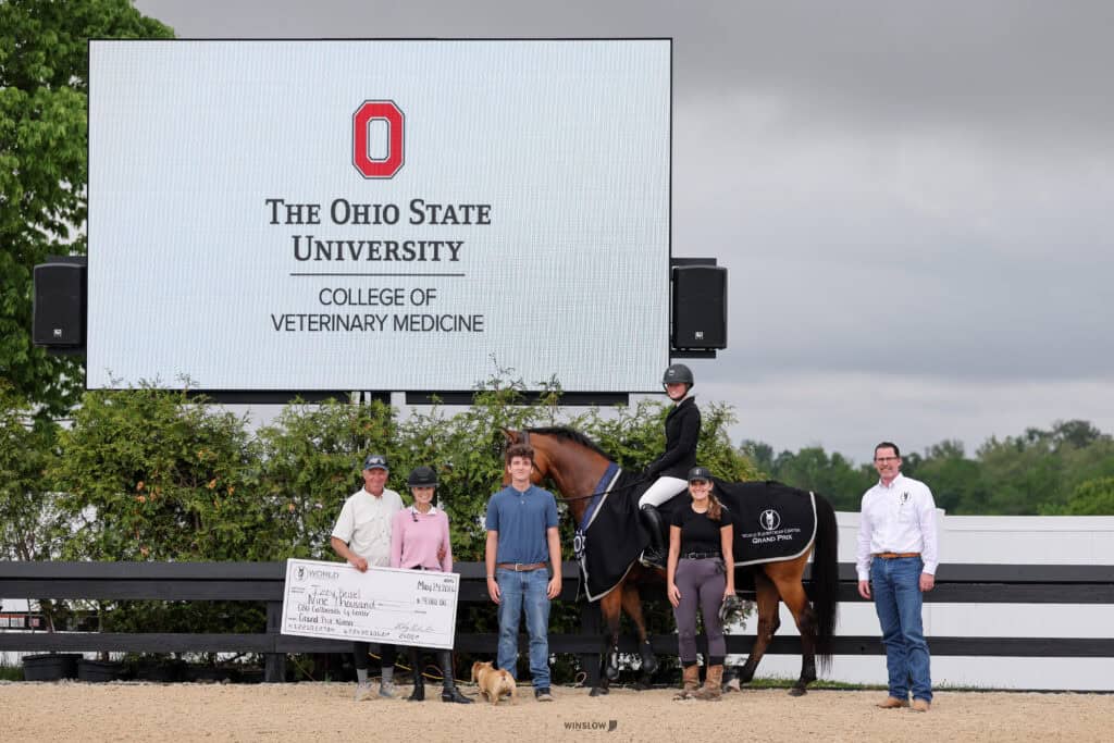 A group of six people and a horse stand in front of a large sign for The Ohio State University College of Veterinary Medicine; one person holds a large check.