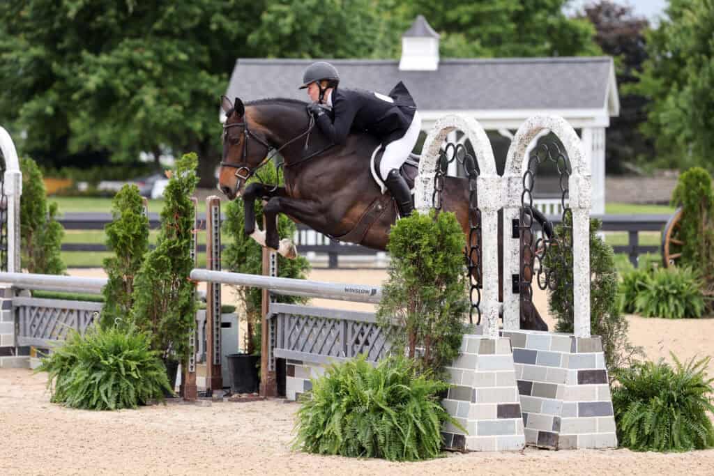 Equestrian rider in formal attire jumps a horse over a stone and wood obstacle during an outdoor competition.