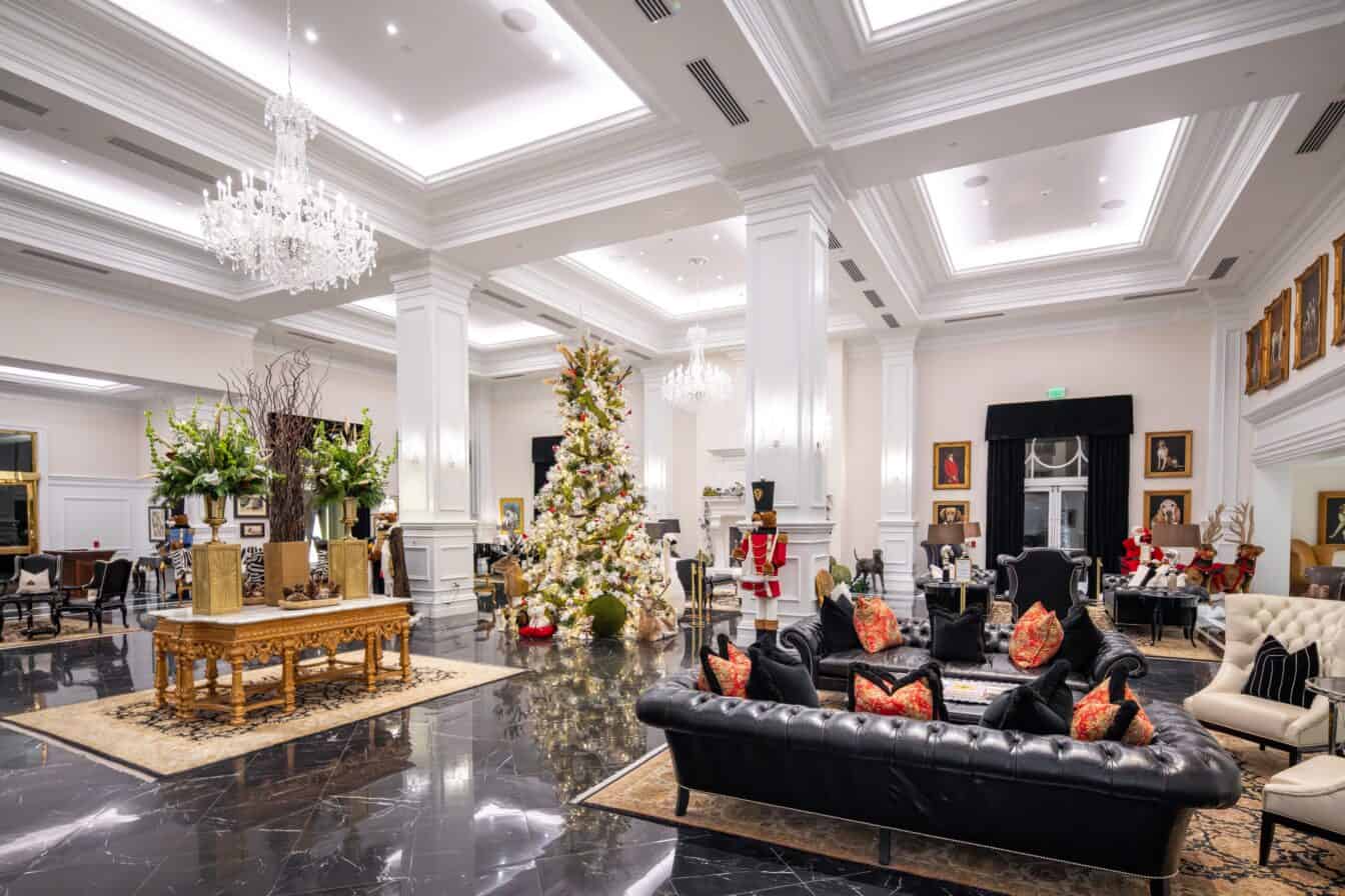 Luxurious hotel lobby with black marble floors, elegant chandeliers, holiday decorations, a large Christmas tree, and plush seating areas.