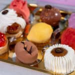An assortment of nine colorful, intricately decorated pastries arranged on a gold tray.
