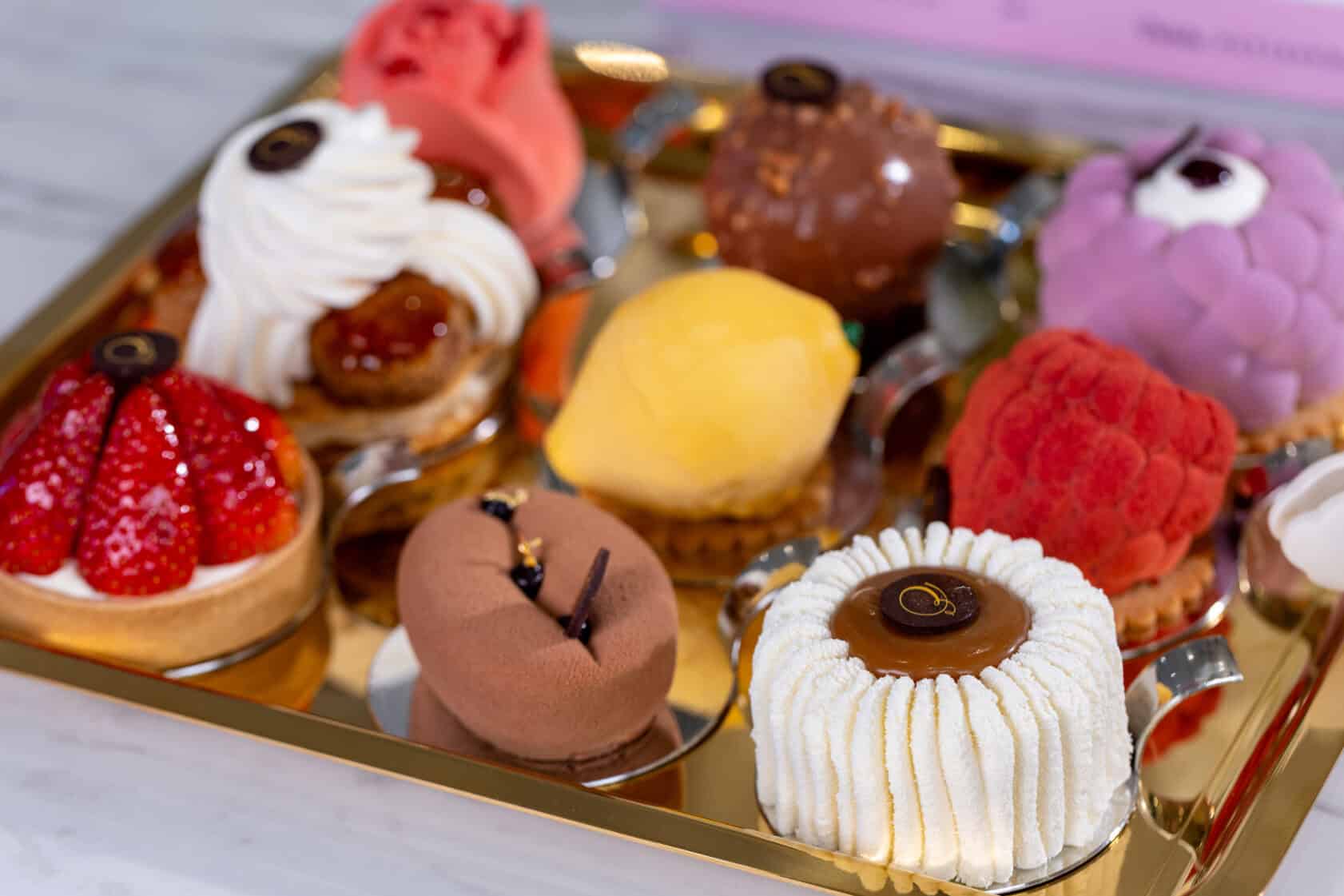 An assortment of nine colorful, intricately decorated pastries arranged on a gold tray.