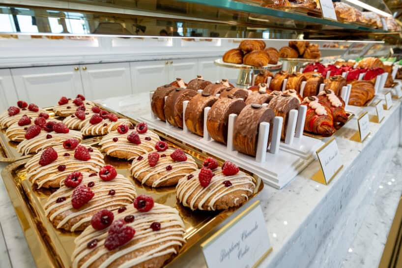 A display of assorted pastries, including croissants and danishes topped with raspberries and icing, arranged on trays in a bakery.
