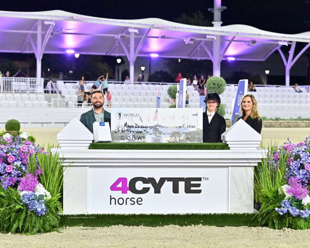 Three people stand behind a large check for $5,000 at an equestrian event, surrounded by flowers and a sign that reads "4CYTE horse.