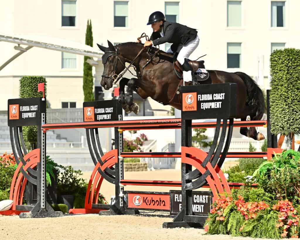A rider in equestrian gear jumps a horse over an obstacle labeled "Florida Coast Equipment" during a show jumping competition.