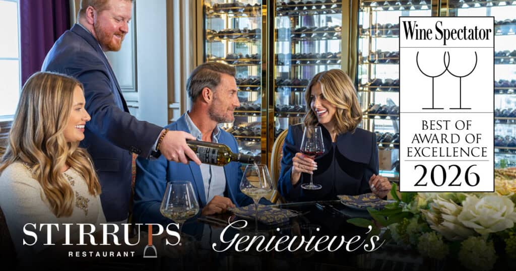 Four people sit at a restaurant table as a server pours wine; a Wine Spectator Best of Award of Excellence 2026 sign is displayed beside them.