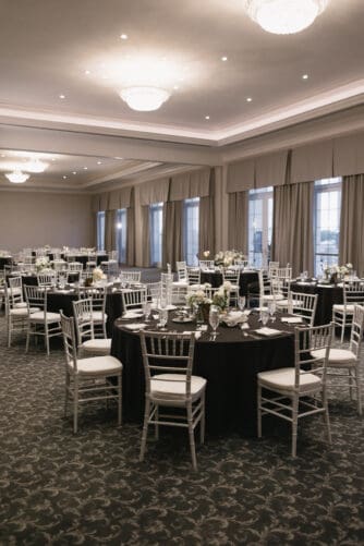 A banquet hall with round tables covered in dark tablecloths, white chairs, and floral centerpieces, set for an event.