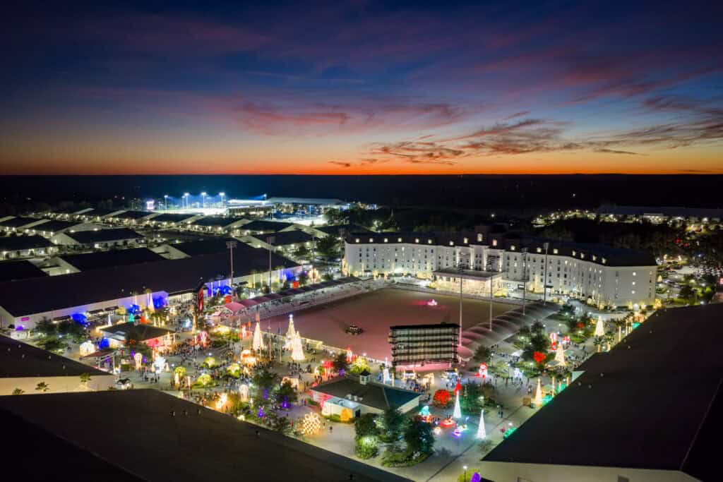Aerial view of a brightly lit complex with holiday decorations at dusk, featuring a large central building and an outdoor plaza under a colorful sunset sky.