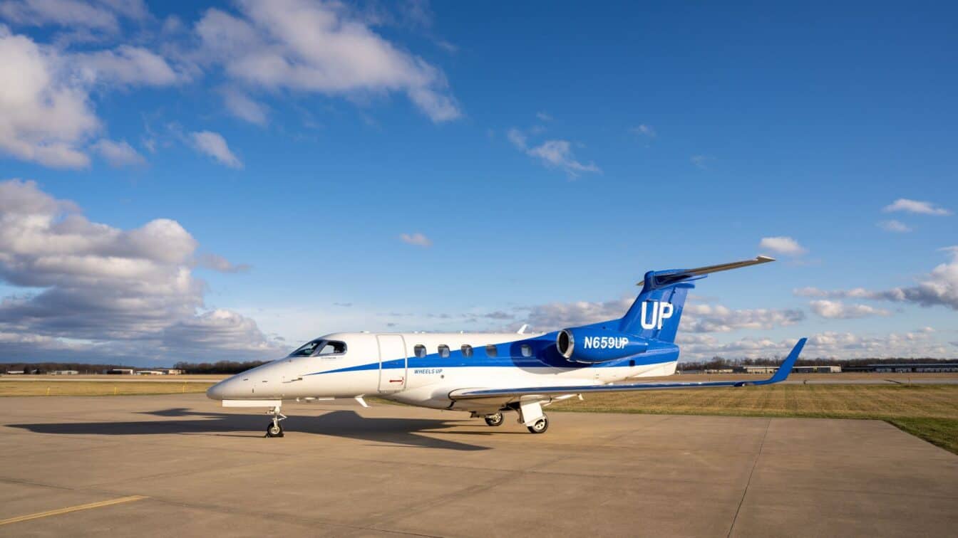 A small blue and white private jet with the tail number N650UP is parked on an airport tarmac under a partly cloudy sky.