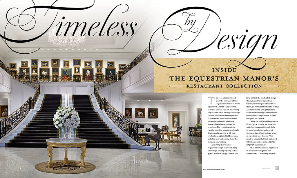 A grand staircase with ornate railings, marble floors, a round table with a white flower arrangement, and framed portraits on the walls in a luxurious, classical interior.