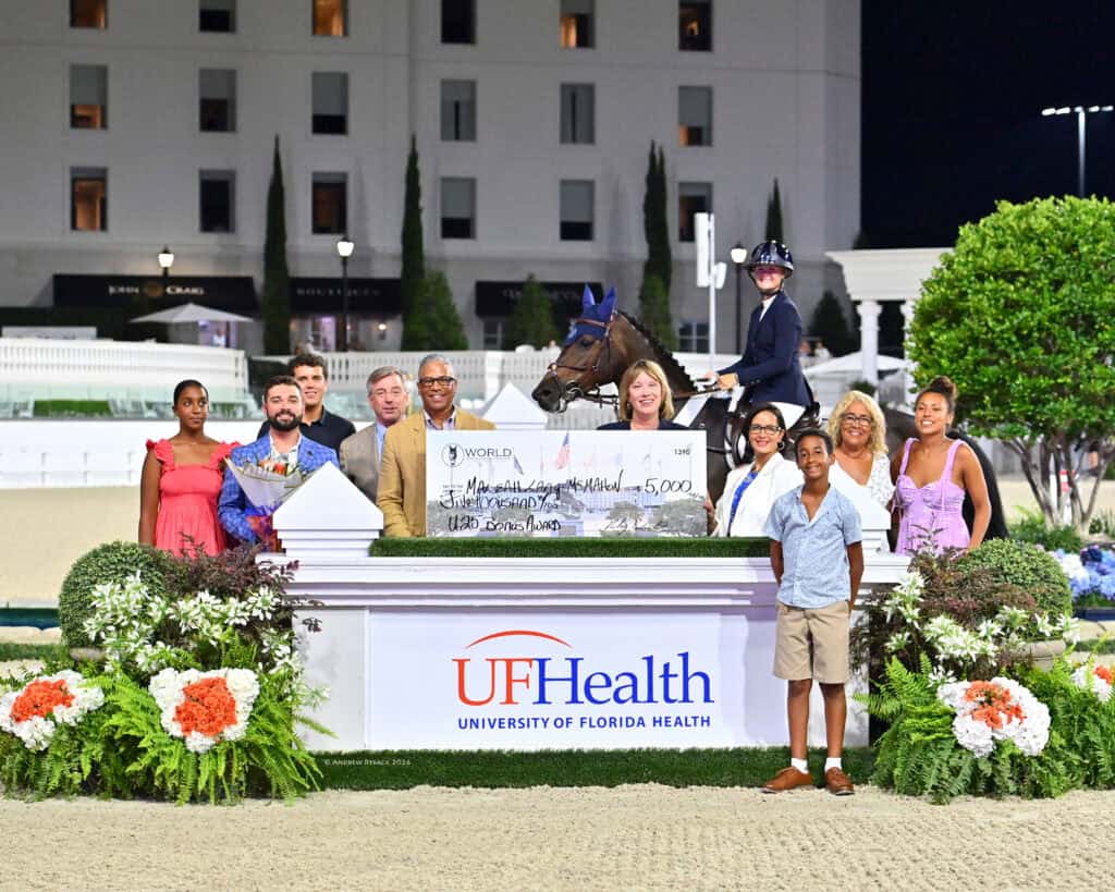 A group of people pose with a ceremonial check and a rider on horseback in front of a UF Health sign at an outdoor event.