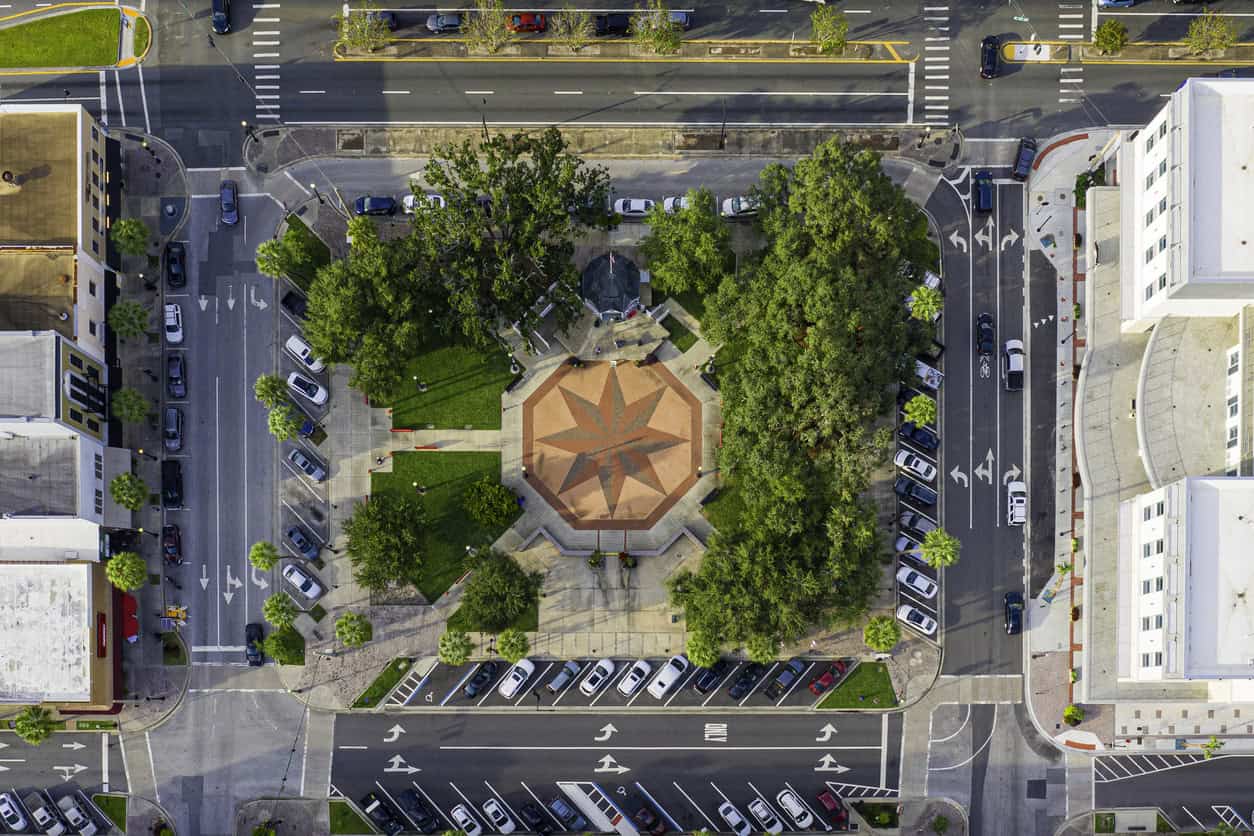Aerial view of a small urban park with a star-shaped central plaza, surrounded by trees, sidewalks, and parked cars along adjacent streets.