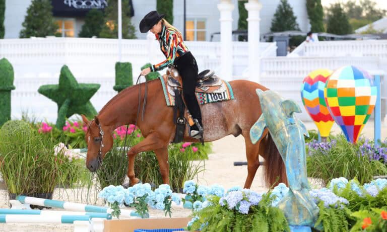 A person in a colorful shirt and black hat rides a brown horse through a decorated obstacle course with flowers and statues.