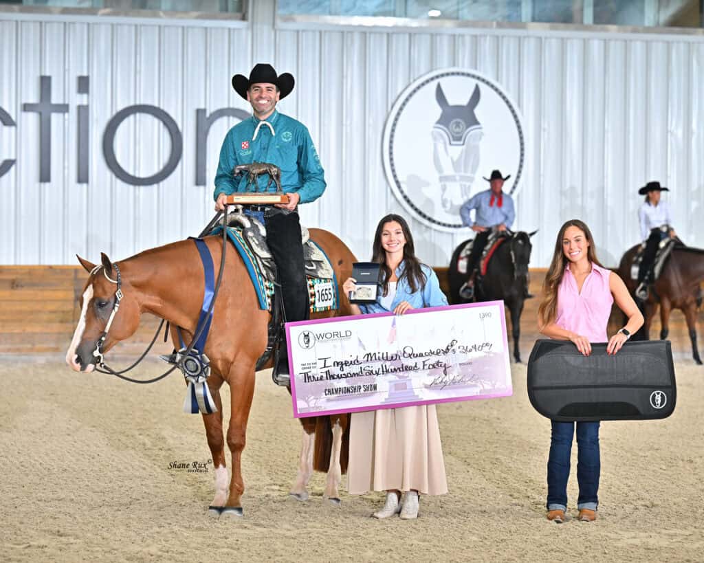 Three people and a horse pose indoors; one man sits on the horse with a trophy, while two women stand holding a large check and a guitar case.