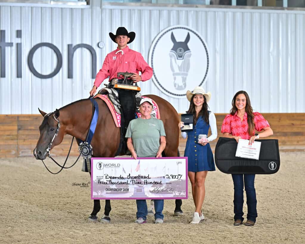 Four people and a horse pose indoors with awards and a large check for $3,900. Two women hold prizes; one man sits on the horse holding a trophy, and a woman stands in front of the horse.