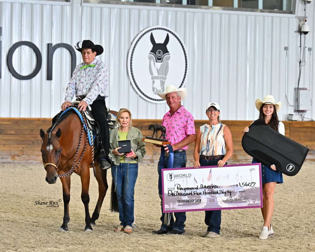 Five people and a horse in an indoor arena; one person on horseback, others hold a trophy, a large check, and a black case. An equestrian logo is visible on the wall behind them.