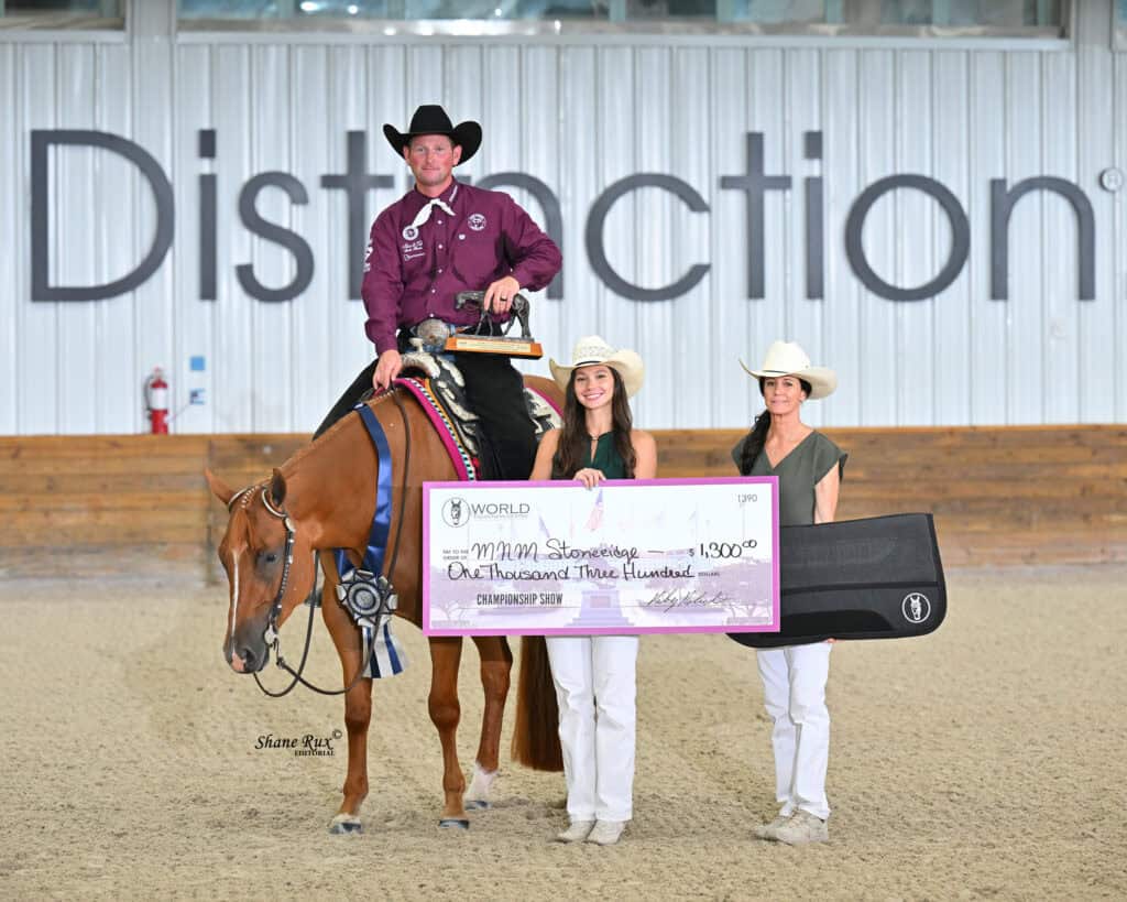 A man on horseback and two women pose indoors with a large prize check for $1,300 and a guitar case.