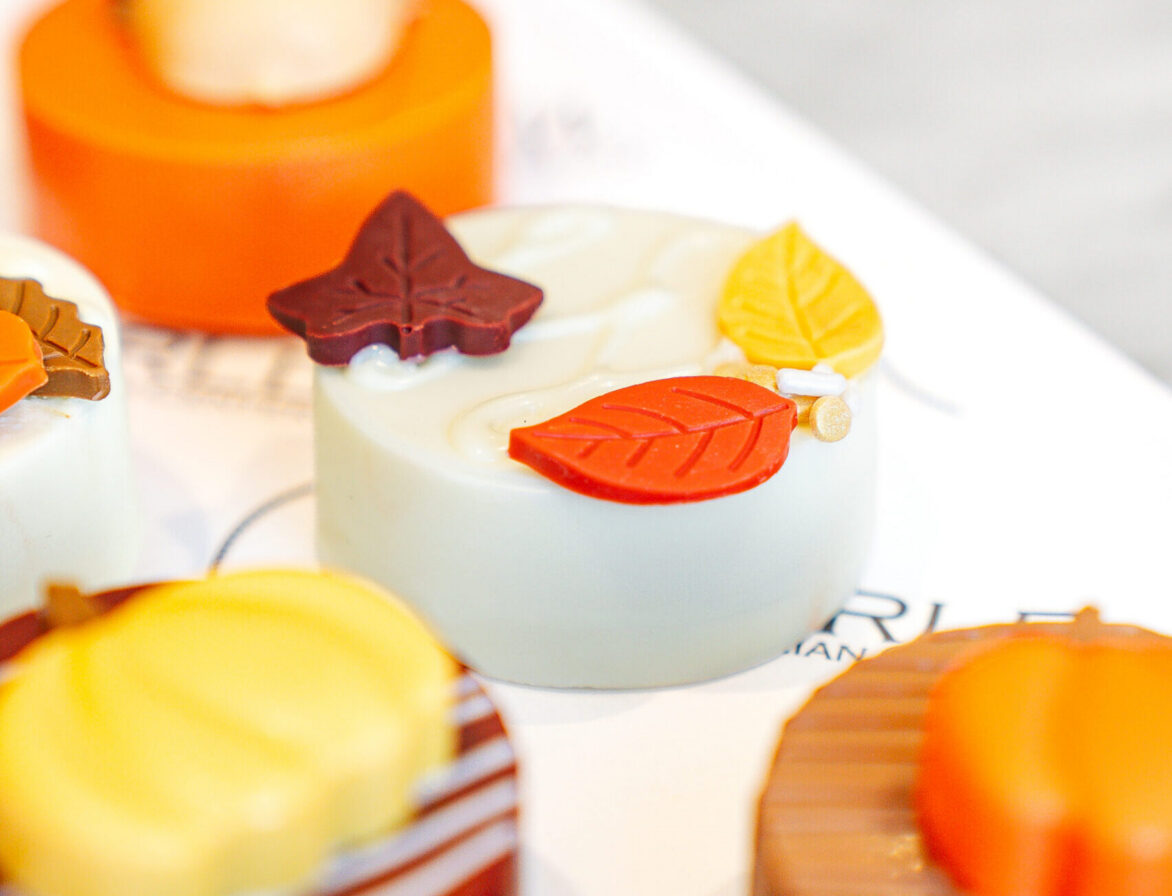Assorted decorative pastries with autumn leaf designs and colorful icing displayed on a white surface.