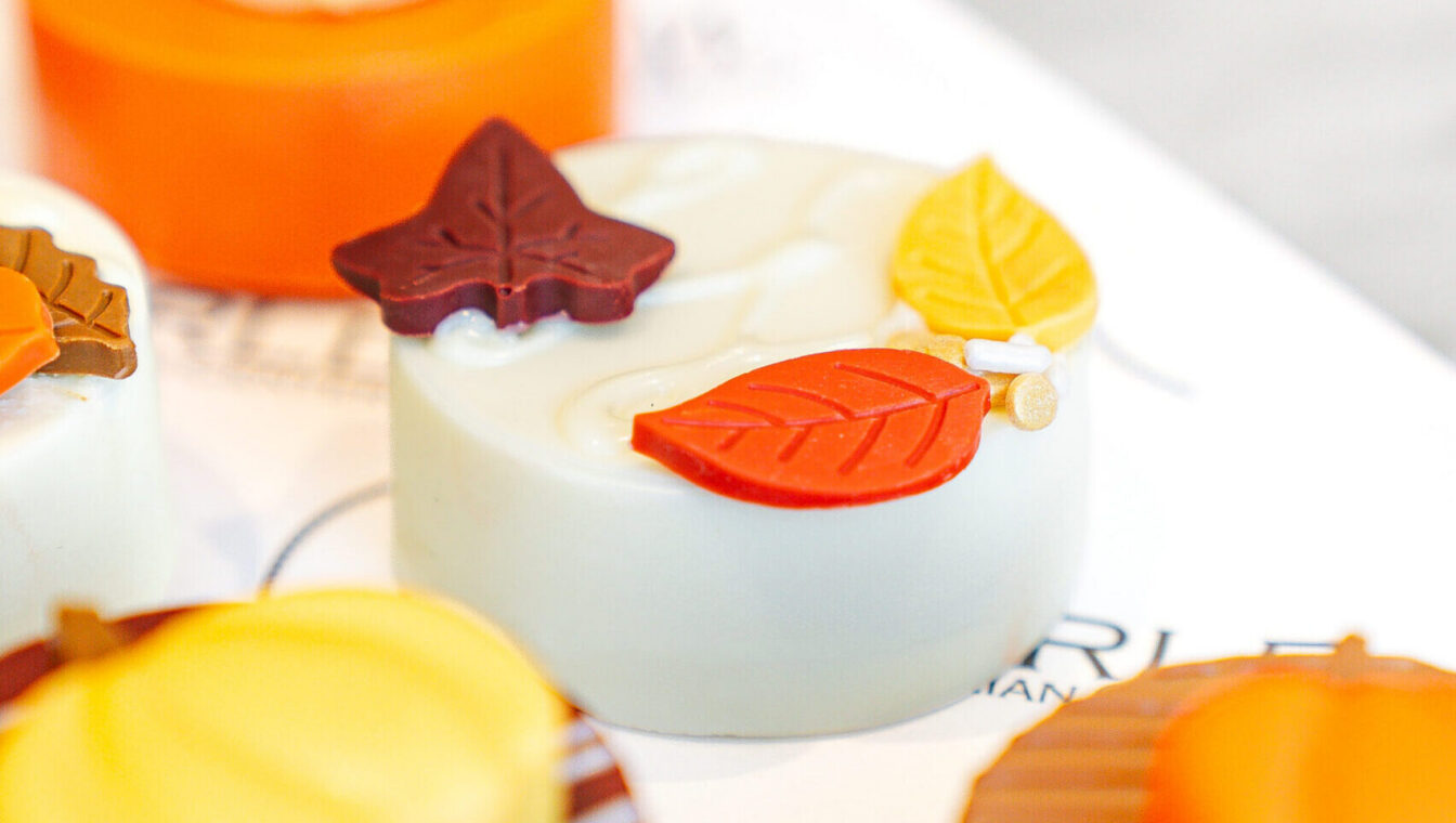 Assorted decorative pastries with autumn leaf designs and colorful icing displayed on a white surface.