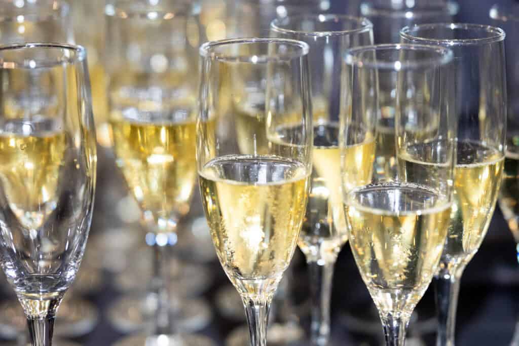 Several champagne flutes filled with sparkling wine are arranged closely together, with bubbles visible in the liquid.