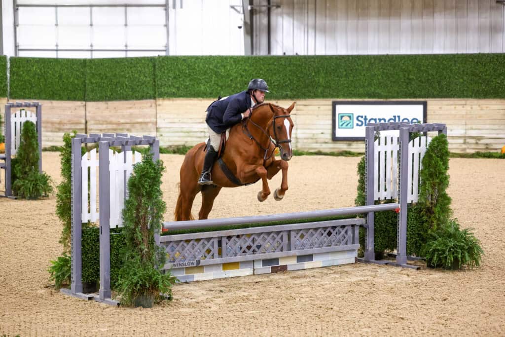 A horse and rider jumping over an obstacle in an indoor arena.