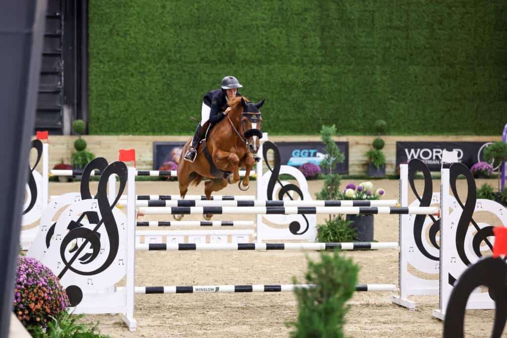 A person in equestrian gear jumping a horse over a hurdle shaped like musical notes.