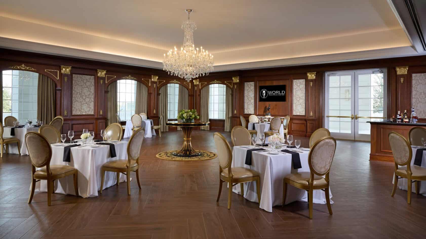 Formal dining room with several square tables set for guests, a large central chandelier, and wood-paneled walls.