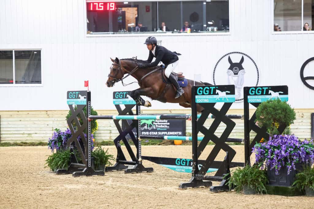 A horse and rider jumping over a hurdle in an indoor arena.